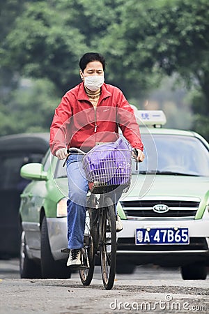 Cyclist with mouth cap with taxi on background, Guangzhou, China Editorial Stock Photo